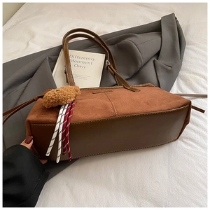 Close-up of retro brown faux suede tote bag with plush bear charm and leather strap detail