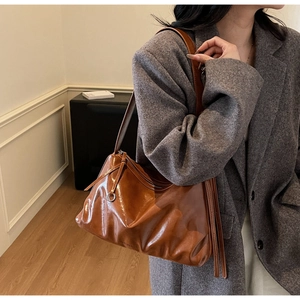 Caramel brown soft tote bag with tassel detail worn over a grey wool coat in a cozy room