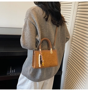 Detail of brown suede handbag featuring embossed letters and a woven handle with beads