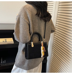 Detail of black suede tote bag featuring woven handles and a colorful beaded charm