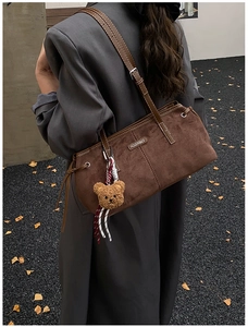 Detail of dark brown suede shoulder bag with plush bear charm and fashion tag