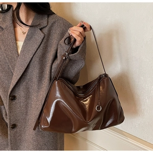 Detail of dark brown glossy leather tote bag shown on model in grey herringbone blazer