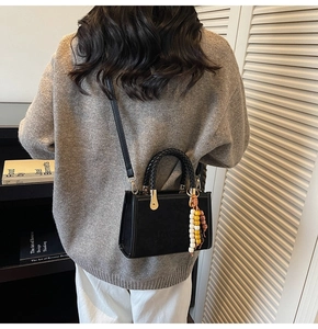 Close-up of black matte suede handbag featuring a woven handle and colorful beaded tassel