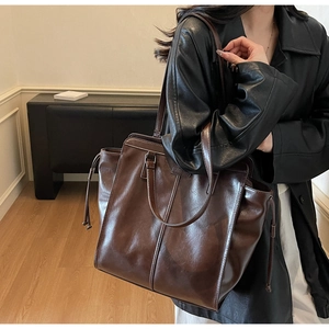 Detail of a large dark brown leather tote bag with drawstrings worn on a shoulder