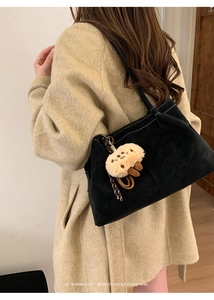 Detail of black suede tote bag with white contrast stitching and plush charm
