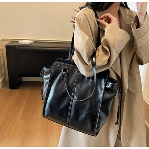 Detail of black faux leather tote bag with drawstring side and stylish metallic hardware