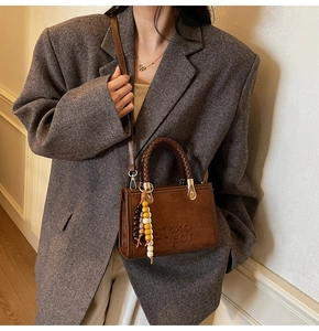 Detail of suede crossbody bag featuring woven handles and colorful bead charm accessory