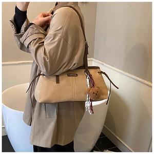 Close-up of beige suede shoulder bag featuring drawstring detail and cute bear charm