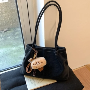 Detail of black matte tote bag with white contrast stitching and plush doll charm