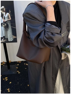 Close-up of a large dark brown litchi grain leather tote bag worn with a wool coat