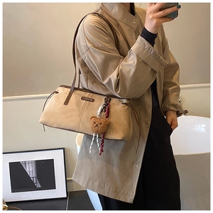Detailed view of beige suede shoulder bag featuring brown leather straps and plush bear charm
