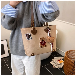 Detail van beige draagtas met bruine lederen handgrepen en beertje als hanger