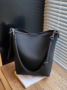 Minimalist black pebble leather bucket bag with adjustable strap on a modern tabletop