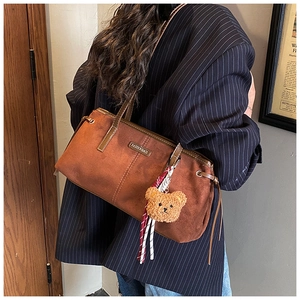 Detail of brown faux suede shoulder bag with bear pendant and fashion logo plate