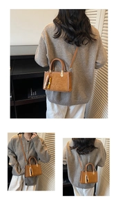Detail view of brown suede handbag with embossed logo and woven top handle on model
