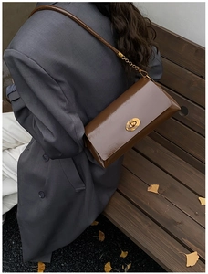 Macro shot of a brown patent leather shoulder bag with a polished gold oval twist lock