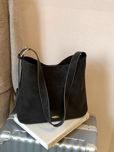 Minimalist matte black large tote bag with gold hardware on a silver suitcase