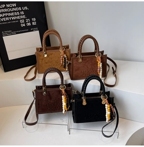 Detail of four suede tote bags in various colors featuring woven handles and beaded charms