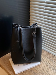 Minimalist black lychee texture bucket bag with adjustable straps on wooden surface