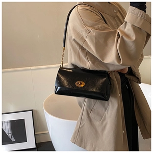 Detail of a vintage black leather shoulder bag with a gold oval twist lock and chain strap