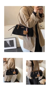 Detail of black faux suede tote bag with brown leather handles and teddy bear charm