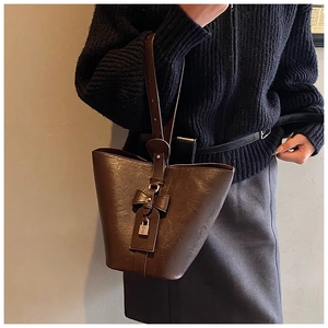 Brown vintage leather bucket bag with bow detail shown on shoulder for sizing