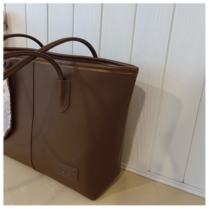 Close-up of dark brown tote bag with vertical stitching and leather fashion logo tag