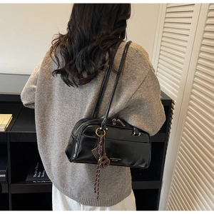 Detail of black glossy leather Boston bag with woven tassel on shoulder of model