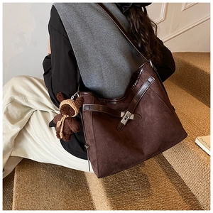 Detail of dark brown matte leather tote bag featuring a cute knitted bear charm on stairs