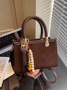 Brown suede tote bag with woven handles and beaded charm in a minimalist office setting
