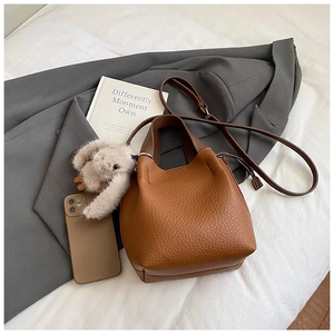 Détail d'un sac seau en cuir marron avec motif litchi et un pendentif lapin en peluche
