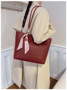 Detail of dark red leather tote bag with elegant floral scarf wrap and brand name plate