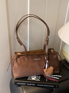 Brown vintage suede shoulder bag with bear charm and adjustable strap on a book