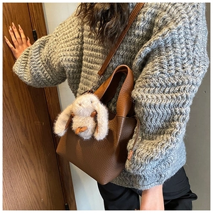 Sac seau en cuir grainé avec breloque lapin en peluche sur fond de pull en maille grise
