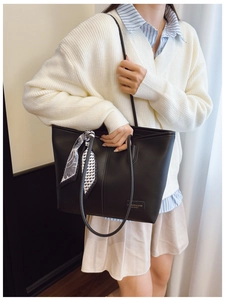 Close-up of black leather tote bag featuring a decorative geometric silk scarf on handle