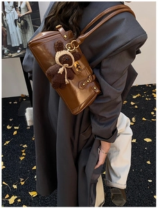 Detail der braunen Schultertasche aus Ölleder mit Bären-Anhänger und Gold-Hardware