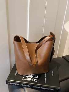 Retro brown leather bucket bag with wide strap on a book, minimalist chic shoulder handbag
