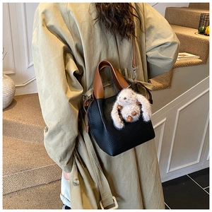 Détail d'un sac seau en cuir grainé noir avec charme lapin blanc et bandoulière marron