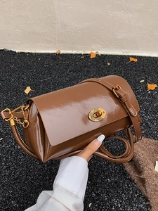 Brown glossy leather shoulder bag with gold twist lock in an autumn street setting