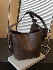 Deep brown leather bucket bag with adjustable wide shoulder strap on a white prop book
