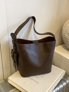 Deep brown vintage leather bucket bag with adjustable strap for women on white book