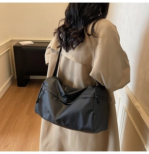 Side view of large black nylon shoulder bag with zipper detail on a beige trench coat