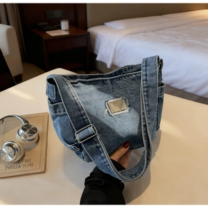 Close-up of washed blue denim crossbody bag featuring metal plate and frayed edges