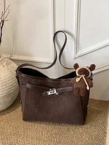 Retro dark brown suede shoulder bag with bear pendant and silver lock on textured rug