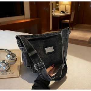 Detail of vintage denim crossbody bag showing distressed metal plate and wide shoulder strap