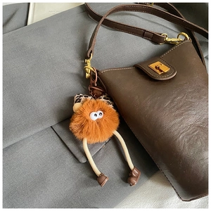 Detail view of coffee leather bucket bag with gold hardware and orange plush monster charm