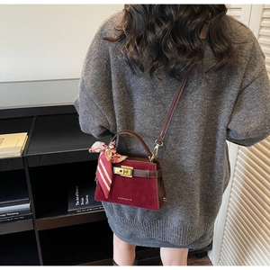 Model wearing dark red matte crossbody Kelly bag with decorative silk scarf on handle