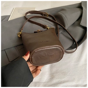 Detail of dark brown leather bucket bag with embossed HOCOMI logo and gold hardware