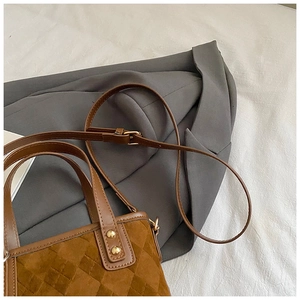 Detail of brown quilted matte bucket bag with golden rivets on a grey suit background