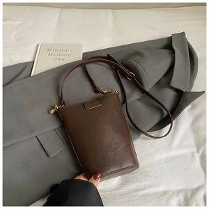 Detailed view of a dark brown leather bucket bag with golden hardware in a lifestyle setting